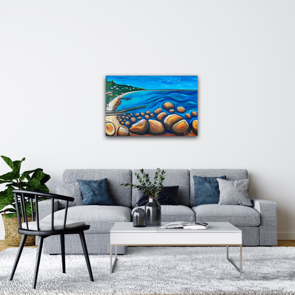 A Calm Day at Flinders Bay displayed above a grey sofa with blue cushions in a bright living room.