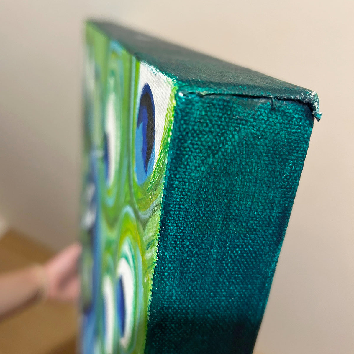 Close-up of the Peacock original canvas, showing its textured teal-painted side and the artwork continuing to the front edge.